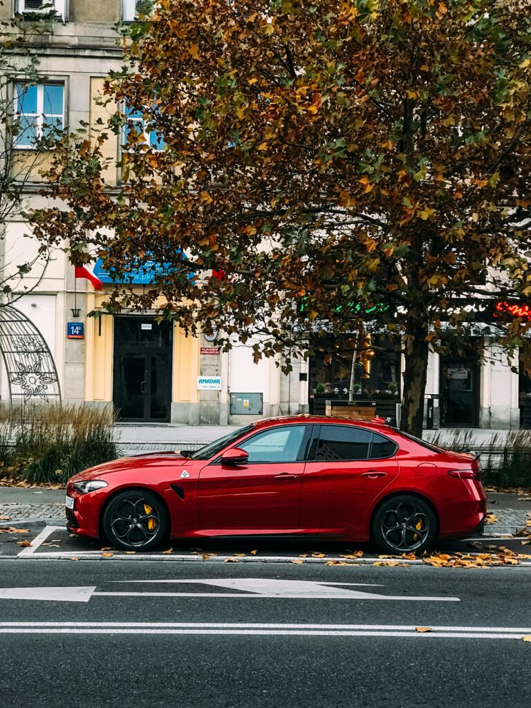 A sleek red sports car parked on a city street lined with autumn trees.